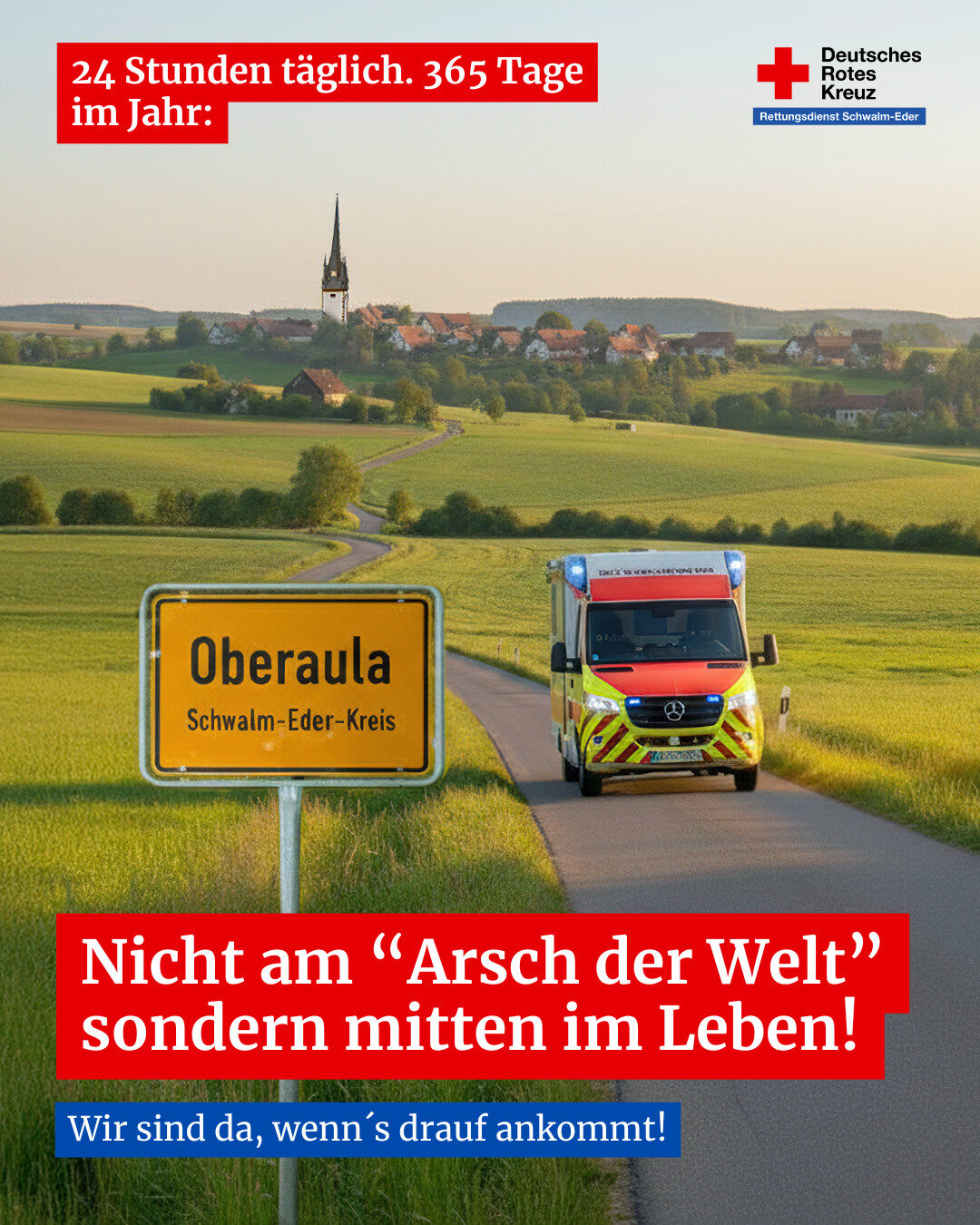Rettungswagen des DRK Schwalm-Eder fährt auf einer Landstraße bei Oberaula durch eine offene Landschaft mit Ortsschild und Kirche im Hintergrund.