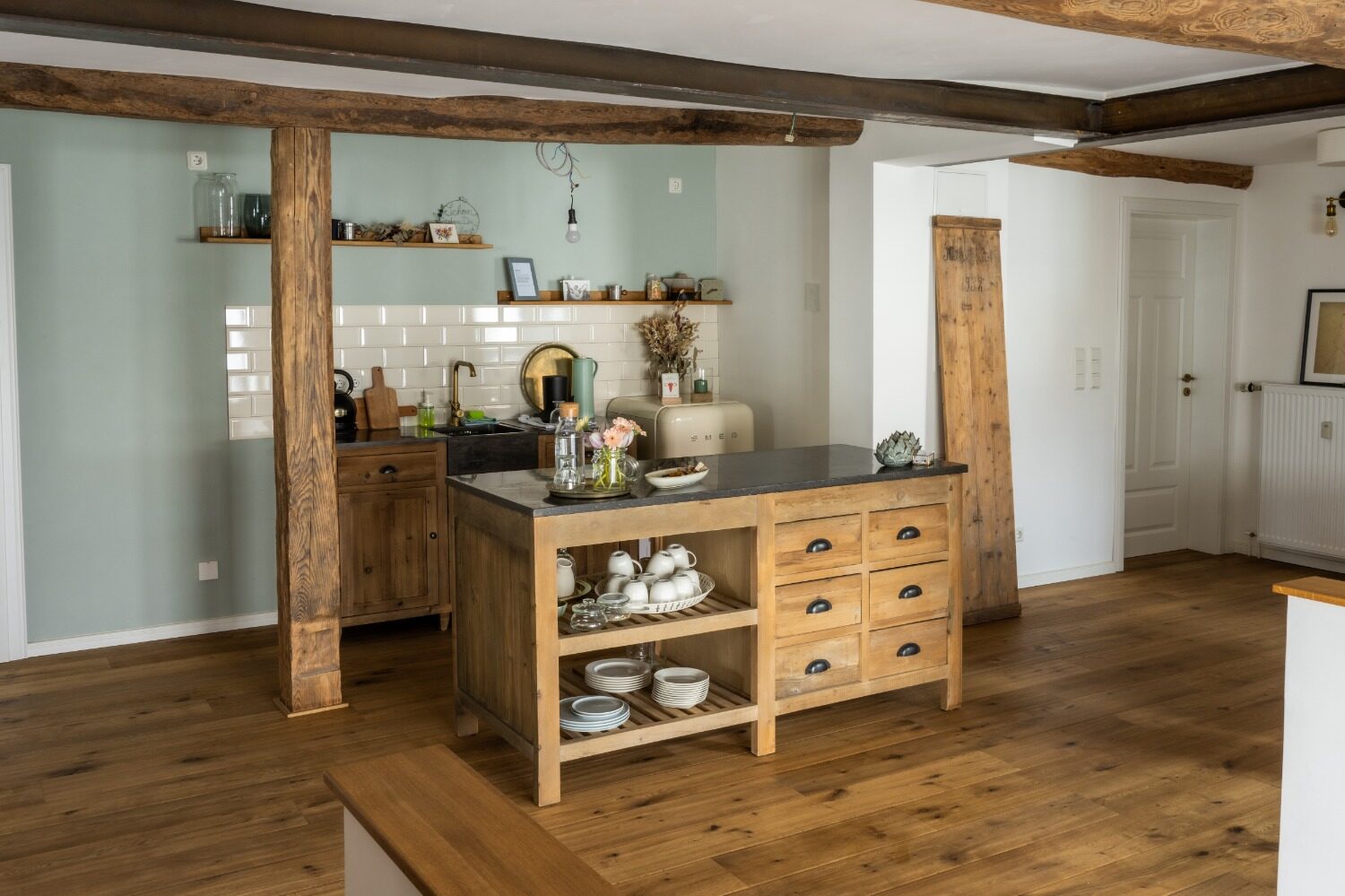 Businessfotografie für Unternehmen: Heller Innenraum mit offen gestalteter Küchenzeile aus Holz, rustikalen Deckenbalken und zentraler Kochinsel, warmes, wohnliches Ambiente mit natürlichen Materialien und aufgeräumter Einrichtung.