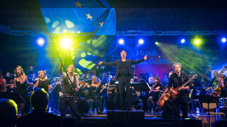 Orchester und Saenger bei einem Konzert auf einer blau ausgeleuchteten Buehne