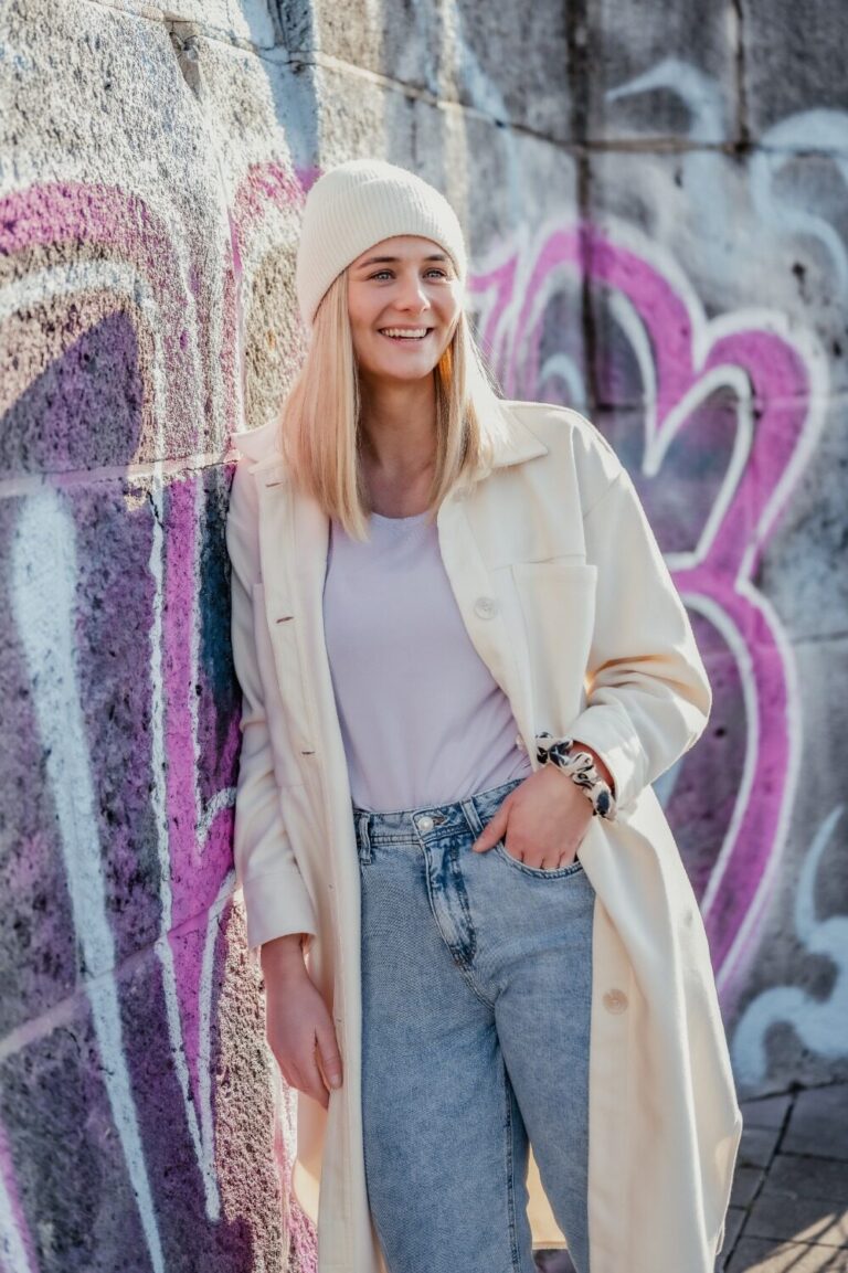 Frau im hellen Mantel vor einer Wand mit Graffiti