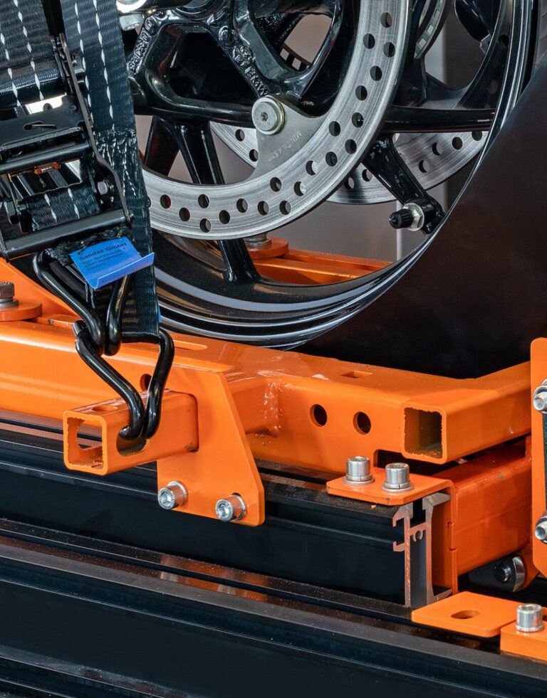Detailaufnahme einer orangefarbenen Maschine mit Rad und Hydraulik