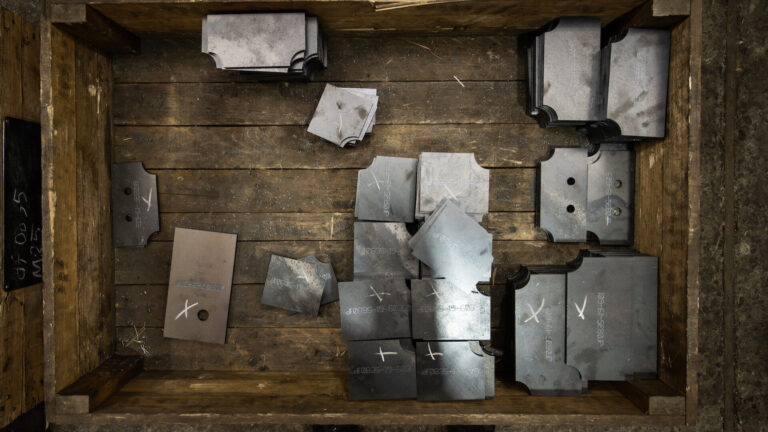 Zugeschnittene Metallteile in einer Holzkiste von oben fotografiert
