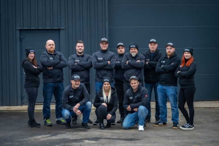 Belegschaft eines Bohrtechnik-Betriebs in Arbeitskleidung vor der Firmenhalle