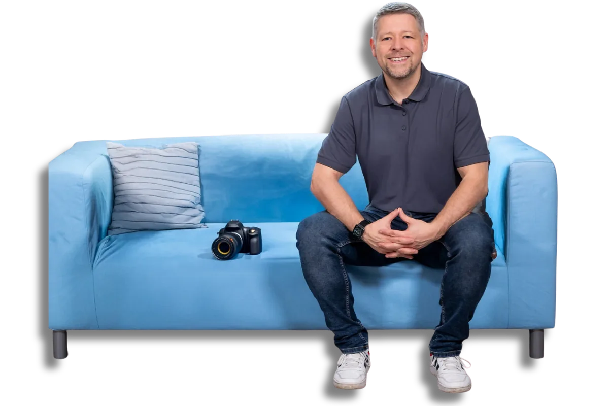 Martin Diebel sitzt auf einem hellblauen Sofa, die H&auml;nde locker gefaltet, neben ihm liegt eine Kamera.