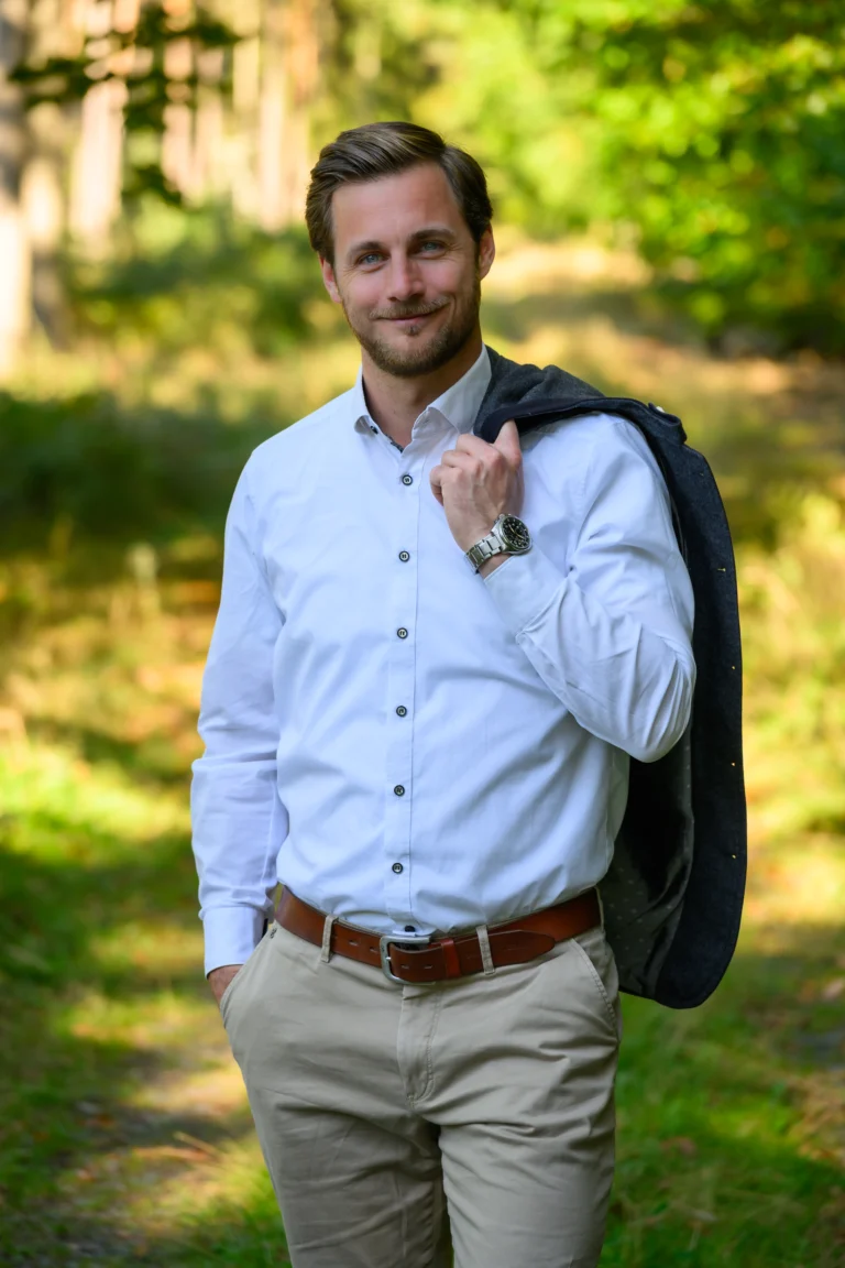 Mann im weissen Hemd mit Sakko ueber der Schulter auf einem Waldweg